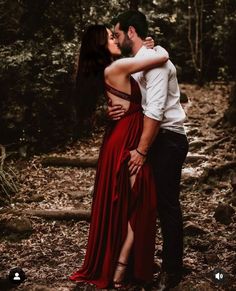 a man and woman are kissing in the woods while wearing long red dresses with high slits