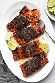 grilled salmon on a white plate with limes and a fork next to it