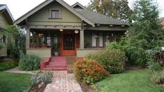 a green house with red steps leading to the front door and flowers on the lawn