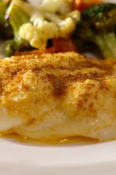 a white plate topped with fish, broccoli and cauliflower covered in sauce