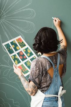 a woman is drawing on the wall with her easel and some stickers in front of her