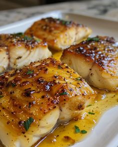 three pieces of fish on a plate covered in sauce and garnished with parsley