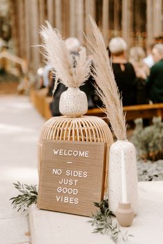 a welcome sign sitting on top of a table next to a vase with some plants in it