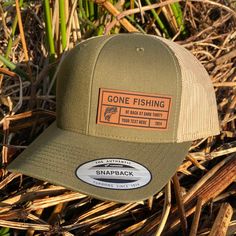 the gone fishing trucker hat is sitting on some grass