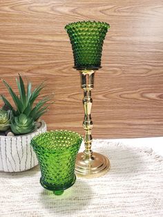 two green glass vases sitting on top of a table next to a potted plant