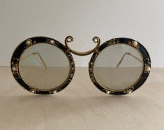 Take a step back in time with these ultra rare Christian Dior sunglasses designed in collaboration with Tura circa 1967. The ornate, yet delicate, enamel cast iron frame has stones shaped as flowers and leaves. Marked 12K GF on arm, indicating that the arms of the glasses are 12k gold filled.  This item its nearly 60 years old and therefore the frame show signs of wear according to age.  Current lenses are prescription, so will need to be replaced. The frames are missing 8 or so of the original decorative stones, which could be repaired by a quality craftsman.  Sold as is. An image from the Tura website history from 1967 shows these exact glasses. Please contact me for any additional questions you may have about this special item. Elegant Metal Sunglasses For Evening, Vintage Gold Round Sunglasses, Vintage Sunglasses With Mirrored Lenses For Evening, Vintage Glass Sunglasses For Evening, Vintage Gold Round Frame Sunglasses, Vintage Round Frame Sunglasses For Party, Vintage Gold Sunglasses With Glass, Elegant Round Glass Sunglasses, Fall Wardrobe Staples