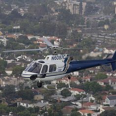 a blue and white helicopter flying over a city with lots of houses in the background