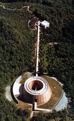 an aerial view of a circular building in the middle of a wooded area with trees around it