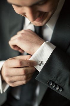 a man in a suit adjusting his cuff on his white shirt and black jacket with silver buttons