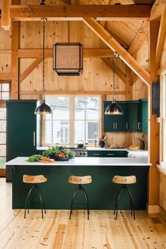 a kitchen with green cabinets and stools next to a counter top on wooden flooring