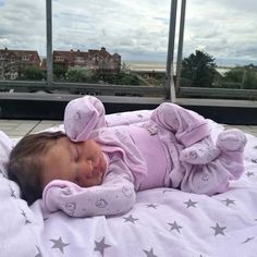 a baby laying on top of a bed next to a window covered in pink and white stars