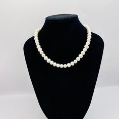 a necklace with white pearls on a black mannequin