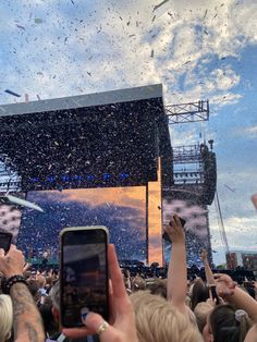 people are taking pictures with their cell phones at an outdoor music festival while confetti is thrown in the air