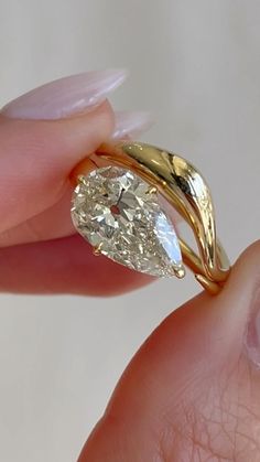 a woman's hand holding an engagement ring with a pear shaped diamond