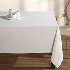 a white table cloth with a teapot on it and two chairs in the background