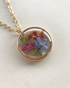 Wildflower Resin Necklace For all my spring lovers! This necklace contains a fern leaf, alyssum flower, golden rod, and a forget me not flower. They are carefully cut and arranged to give you a beautiful combination of colors. It is then preserved in layers of resin and cured for a period of 2-3 days. Pendant size is about the size of a dime.  Please keep in mind that although I try my best to eliminate any visible bubbles, you will still see a few micro bubbles in this piece.  Necklace chain, j Delicate Round Flower Necklace With Pressed Flowers, Delicate Round Pressed Flower Necklace, Delicate Round Necklace With Pressed Flowers, Delicate Round Necklaces With Pressed Flowers, Rose Gold Necklace With Pressed Flowers, Yellow Gold Flower Jewelry With Pressed Flowers, Yellow Gold Flower-shaped Jewelry With Pressed Flowers, Yellow Gold Jewelry With Pressed Flowers, Dainty Pressed Flowers Necklace For Anniversary