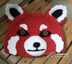 a crocheted red bear hat sitting on top of a wooden bench with eyes wide open