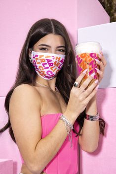 a woman wearing a face mask and holding up a cup of coffee with the word donut printed on it