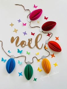 the word noel is surrounded by colorful paper decorations and butterfly shapes on a white surface