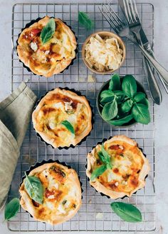 several small pizzas with spinach leaves and cheese on top sit on a cooling rack