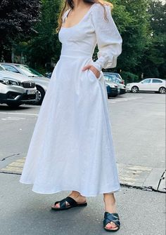 a woman in a white dress is standing on the street with her hands on her hips