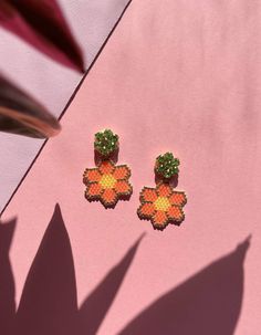 two pairs of earrings on top of a pink table next to a potted plant