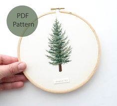 a hand is holding up a cross stitch pattern with a small pine tree on it