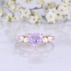 a pink sapphire and diamond ring with three white diamonds on the side, in front of some flowers