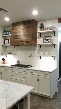 a kitchen with white cabinets and marble counter tops, open shelving above the stove