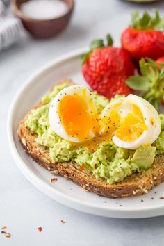 an egg and avocado toast on a plate with strawberries next to it