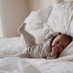 a baby laying on top of a bed with white sheets and pillows in it's arms