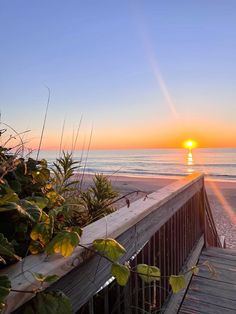 the sun is setting over the ocean and beach as seen from a wooden walkway that leads to the beach