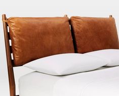 a bed with white sheets and brown leather headboard