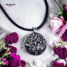 a close up of a necklace on a table with flowers in the foreground and a white background