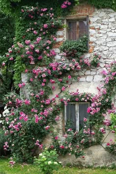 an old stone building with pink flowers growing on it's side and windows in the wall