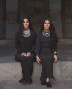 two women in black dresses sitting next to each other on concrete steps with their hands together