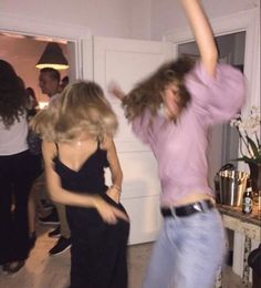 two women are dancing in a room with other people