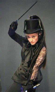 a woman dressed in black with a top hat holding a wand and posing for the camera