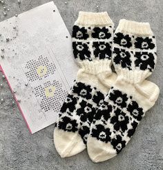 two pairs of black and white knitted socks next to a cross stitch pattern book