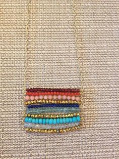 a multicolored beaded necklace is hanging on a gold chain and it's attached to a white fabric