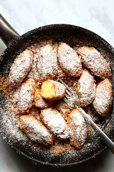 powdered sugar covered pastries are in a skillet with a fork and spoon