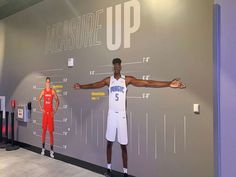 a man standing in front of a wall with measurements on it and two mannequins behind him