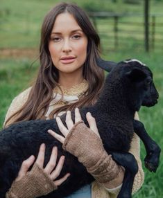 a woman holding a black sheep in her hands