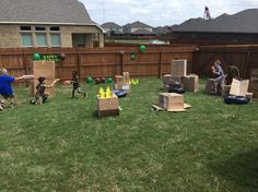 a group of dogs playing in the yard with boxes on the ground and people standing around