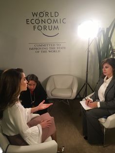 two women sitting in chairs talking to each other while another woman stands behind them and looks at the camera