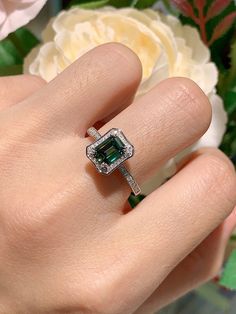 a woman's hand holding a ring with an emerald colored stone in the center