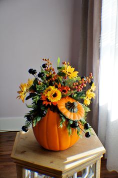 a pumpkin filled with flowers sitting on top of a wooden table next to a window