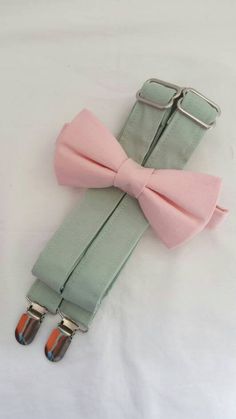 a pink bow tie laying on top of a light green suspender with matching clips