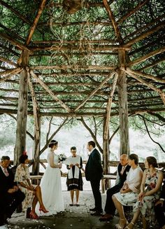 a group of people standing around each other in front of a wooden structure with trees