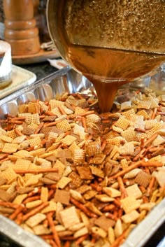 a person pouring some kind of liquid into a pan filled with cheesy crackers